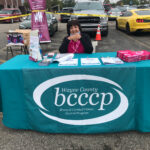 Woman sitting at outdoor booth for Breast & Cervical Cancer Control Program