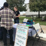 Woman helping visitors at outdoor booth for Mental Health & Welness